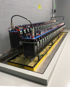 2 long rows of batteries on racks above spill containment and batteries with Eagle Eye Power Solutions Vigilant battery monitoring system attached