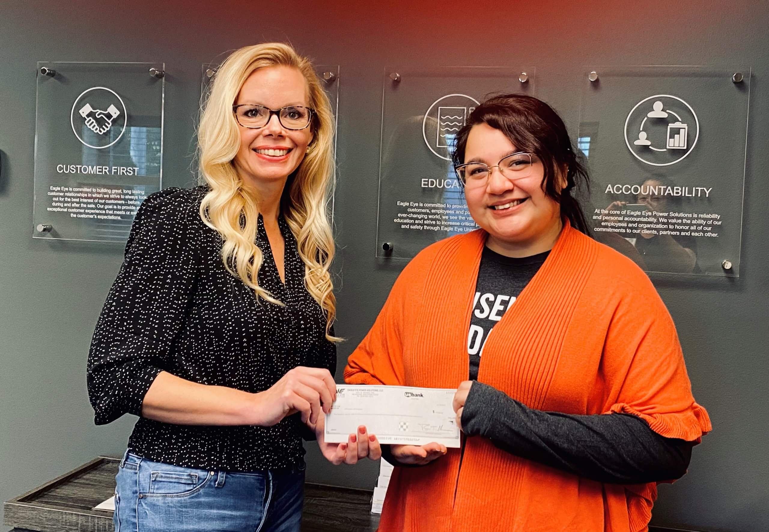 Marketing Coordinator Marlie Antonic handing a check from Eagle Eye Power Solutions to a representative of Advocates of Ozaukee.