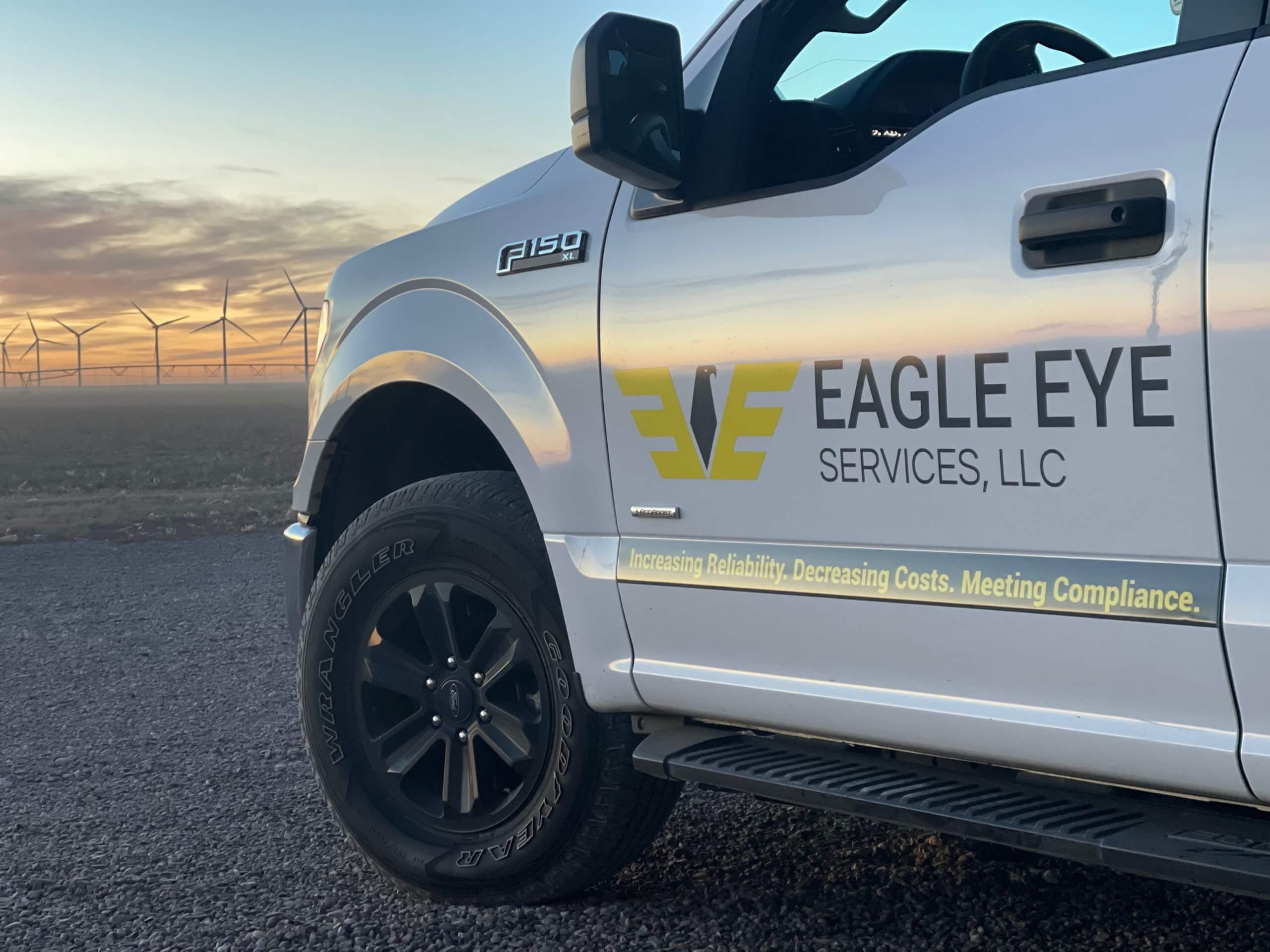 Eagle Eye Services truck parked in front of a windmill farm at sunset.