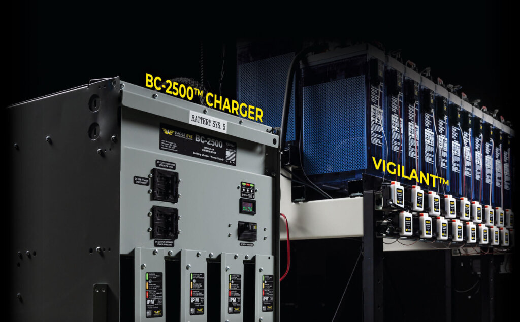 A close-up of Eagle Eye Power Solutions' BC-2500™ Charger alongside a row of batteries equipped with VIGILANT™ monitoring devices, showcasing advanced battery charging and monitoring technology for critical power systems.