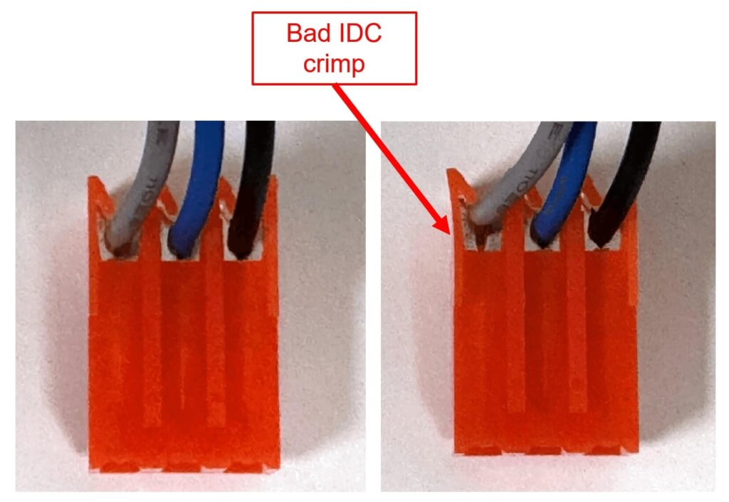 Close-up comparison of two orange IDC (Insulation Displacement Connector) terminals with three inserted wires—gray, blue, and black. The left image shows a proper crimp, while the right image highlights a "Bad IDC crimp" with an arrow pointing to the improperly seated gray wire. This demonstrates an incorrect connection that may lead to electrical issues.