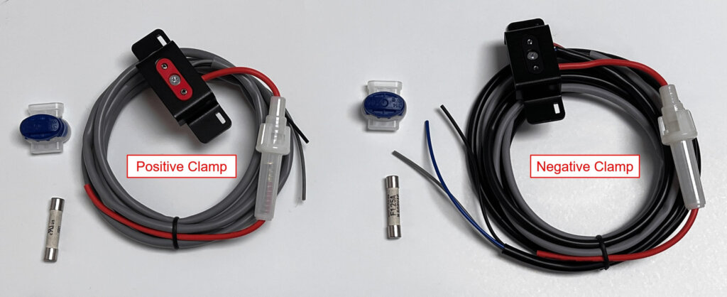 Image showing the components for installing Vigilant® battery sensor cable clamps. On the left is the Positive Clamp with a red plastic housing, gray and red wires, and accompanying parts including a fuse and gel splice connector. On the right is the Negative Clamp with a black plastic housing, black, red, and blue wires, also with a fuse and splice connector. Both sets are coiled and labeled accordingly.