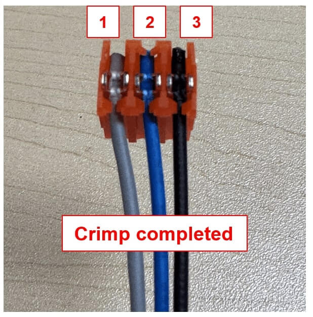 Close-up image of a completed IDC (insulation displacement connector) crimp with three wires inserted into positions labeled 1, 2, and 3. The gray wire in Position 1 is one of the black sense wires from the negative post, the blue wire in Position 2 is the sense wire from the same post, and the black wire in Position 3 is one of the gray pulse wires. The crimp is secured, and the connector is labeled "Crimp completed" at the bottom.