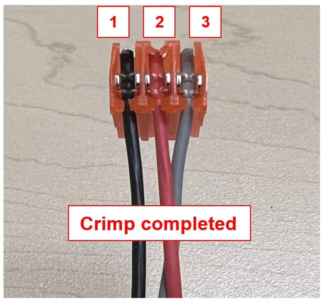 Close-up image of a completed IDC (Insulation Displacement Connector) crimp showing three wires secured into positions labeled 1, 2, and 3. The wires include a black sense wire (position 1), a red sense wire (position 2), and a gray pulse wire (position 3), all inserted into a translucent orange GRY IDC connector. A label below the connector reads “Crimp completed.” The image demonstrates the correct wire order for the first sensor in the system installation.