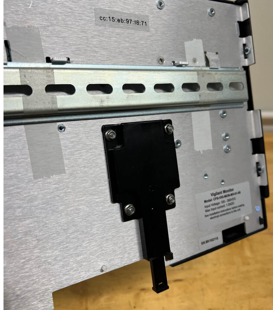 Rear view of an Eagle Eye Power Solutions Vigilant battery monitor, highlighting the black DIN rail clip mounted on the metal enclosure for secure installation. Labels with MAC address and device specifications are also visible.