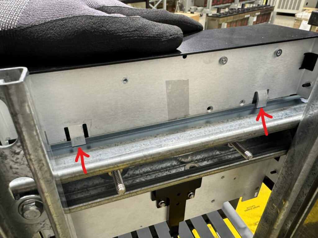 Back view of a Vigilant® monitor being installed onto a DIN rail, with two red arrows pointing to the metal tabs that must be aligned and seated onto the top edge of the DIN rail. A gloved hand holds the monitor in position.