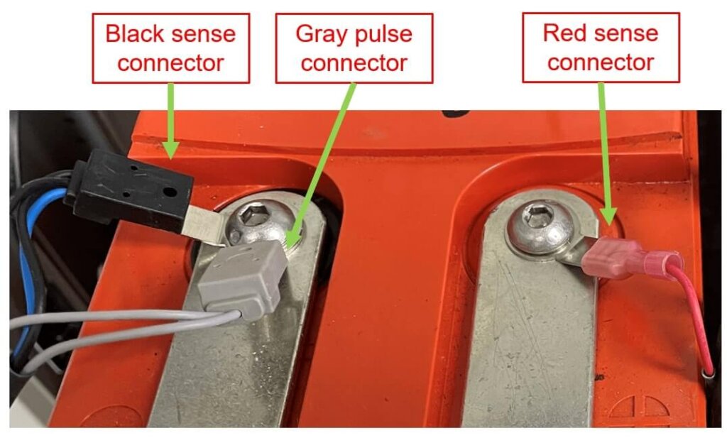 A battery terminal with standoff hardware is shown with three connectors: a black sense connector attached to the negative post, a gray pulse connector attached to the same negative post, and a red sense connector attached to the positive post. Each connector is clearly labeled and securely fastened to a tab washer.