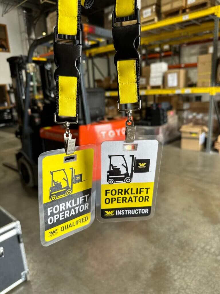Close-up of Eagle Eye Power Solutions forklift operator and instructor badges hanging on yellow lanyards, with a forklift and warehouse shelves in the background, highlighting workplace safety and certification standards.