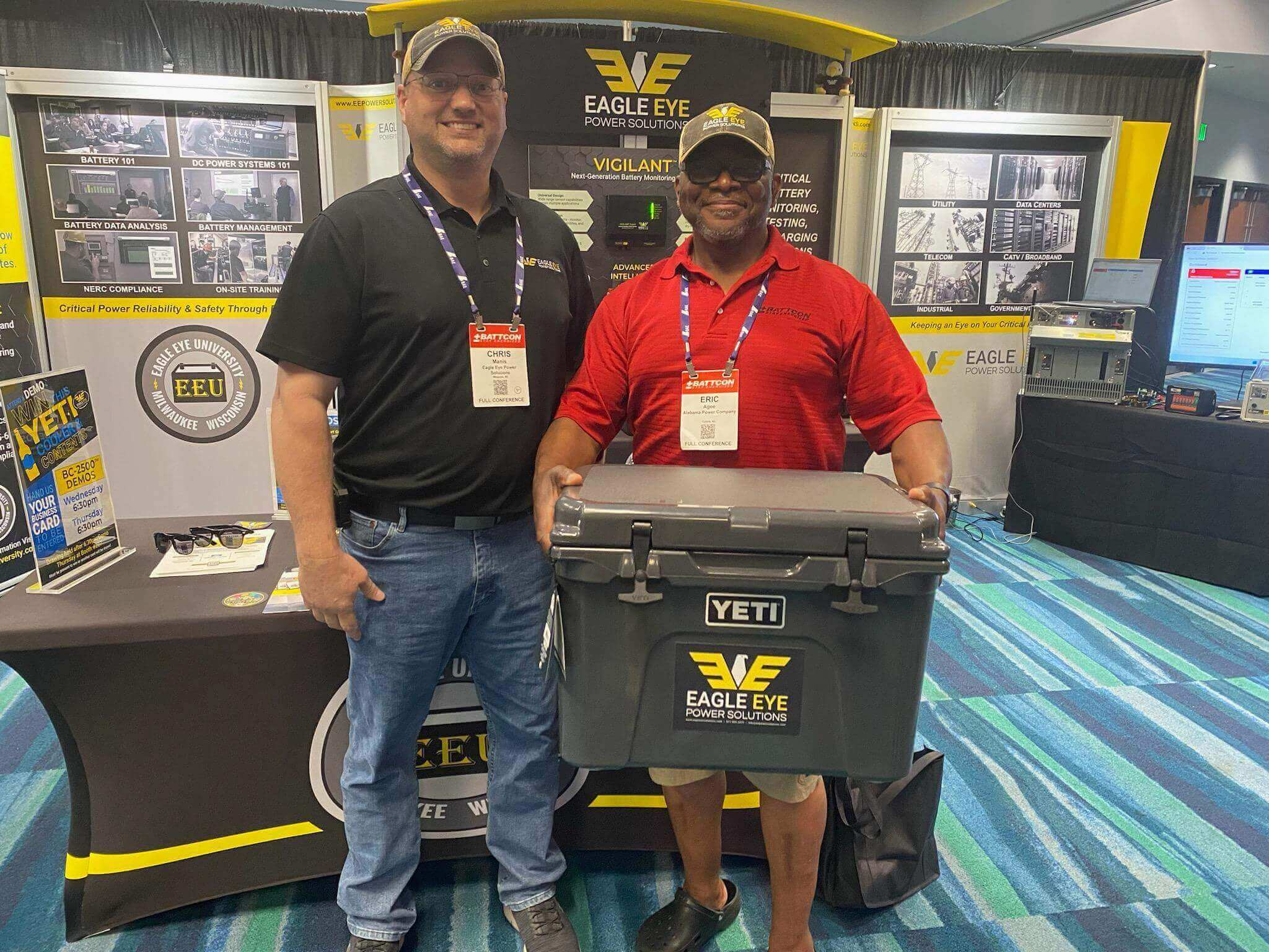 Chris Manis, Regional Sales Manager for Eagle Eye Power Solutions, stands with a smiling customer who just won a Yeti cooler at a tradeshow, showcasing Eagle Eye's commitment to customer engagement and satisfaction.