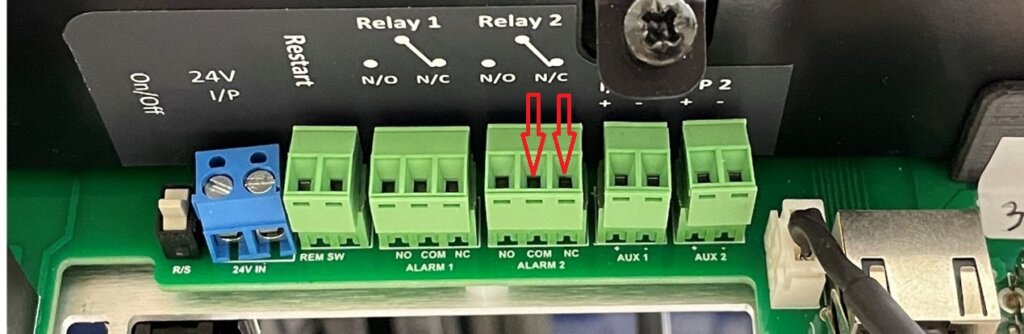 Close-up view of the relay terminal block on the Eagle Eye Power Solutions Vigilant® battery monitor. The green terminal labeled "Relay 2" is highlighted with red arrows pointing to the NC (Normally Closed) and C (Common) terminals, which are used for the Watchdog Alarm wiring. Labels and connection points for other relays and auxiliary inputs are also visible.