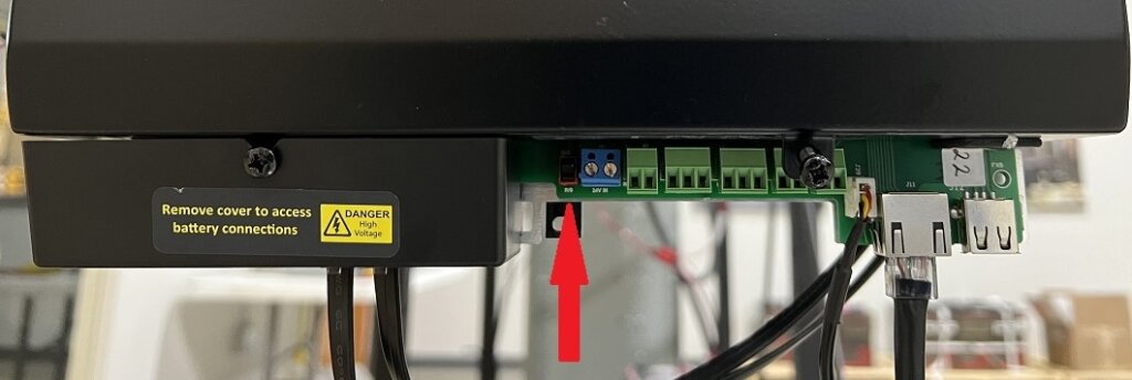 Image of the underside of a Vigilant® monitor from Eagle Eye Power Solutions with the front right cover removed. A red arrow points to the power switch, which needs to be flipped down to turn the monitor on.