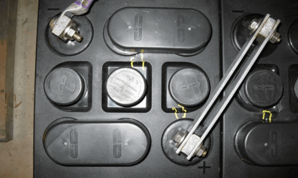 Battery cell showing signs of positive plate growth with bulging covers and compromised seals, highlighting mechanical stress and potential leakage points.