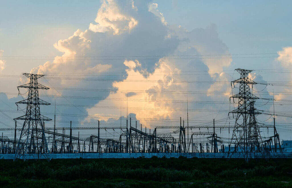 Power transmission infrastructure at a Dominion Energy power substation, silhouetted against a dramatic sunset sky with towering cloud formations.